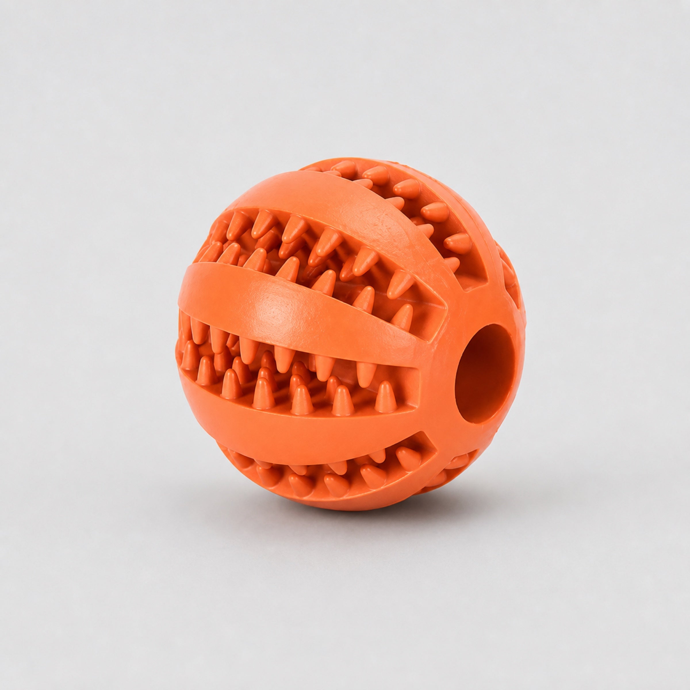Orange rubber dog chew ball dental cleaning treat toy on light grey background